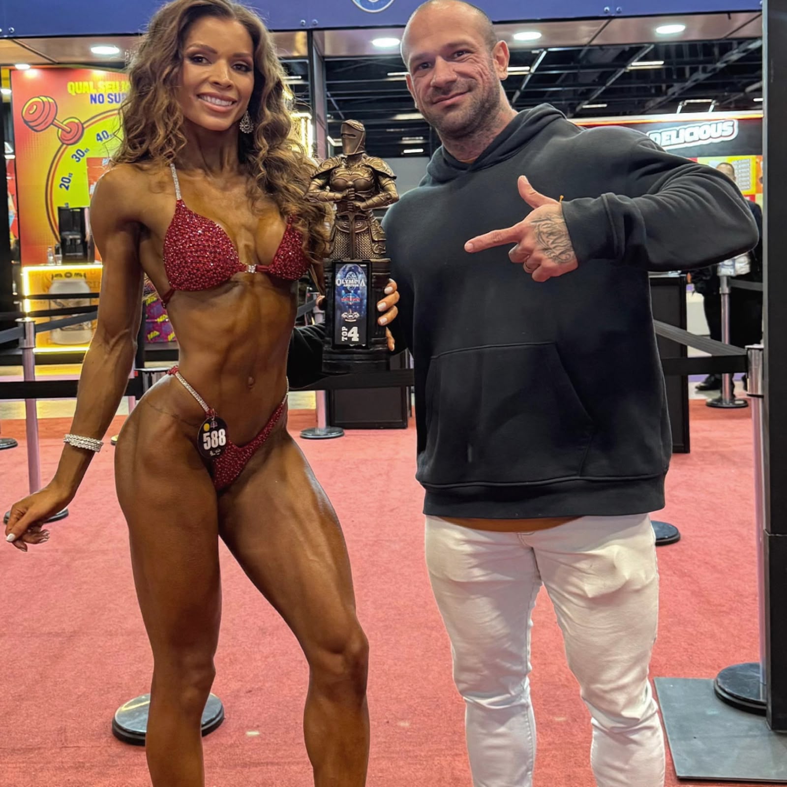 Joel ao lado de uma atleta com um troféu em um evento de fisiculturismo