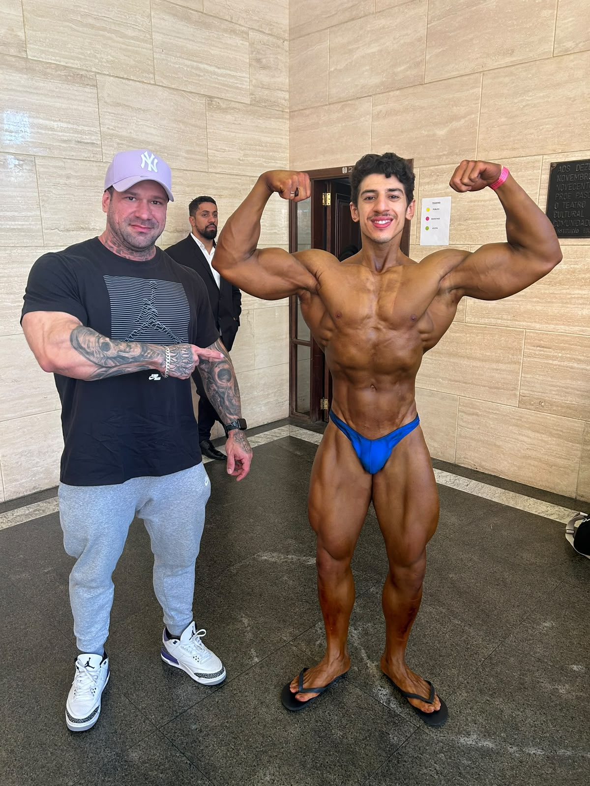 Joel ao lado de um atleta em pose de fisiculturismo nos bastidores de um evento