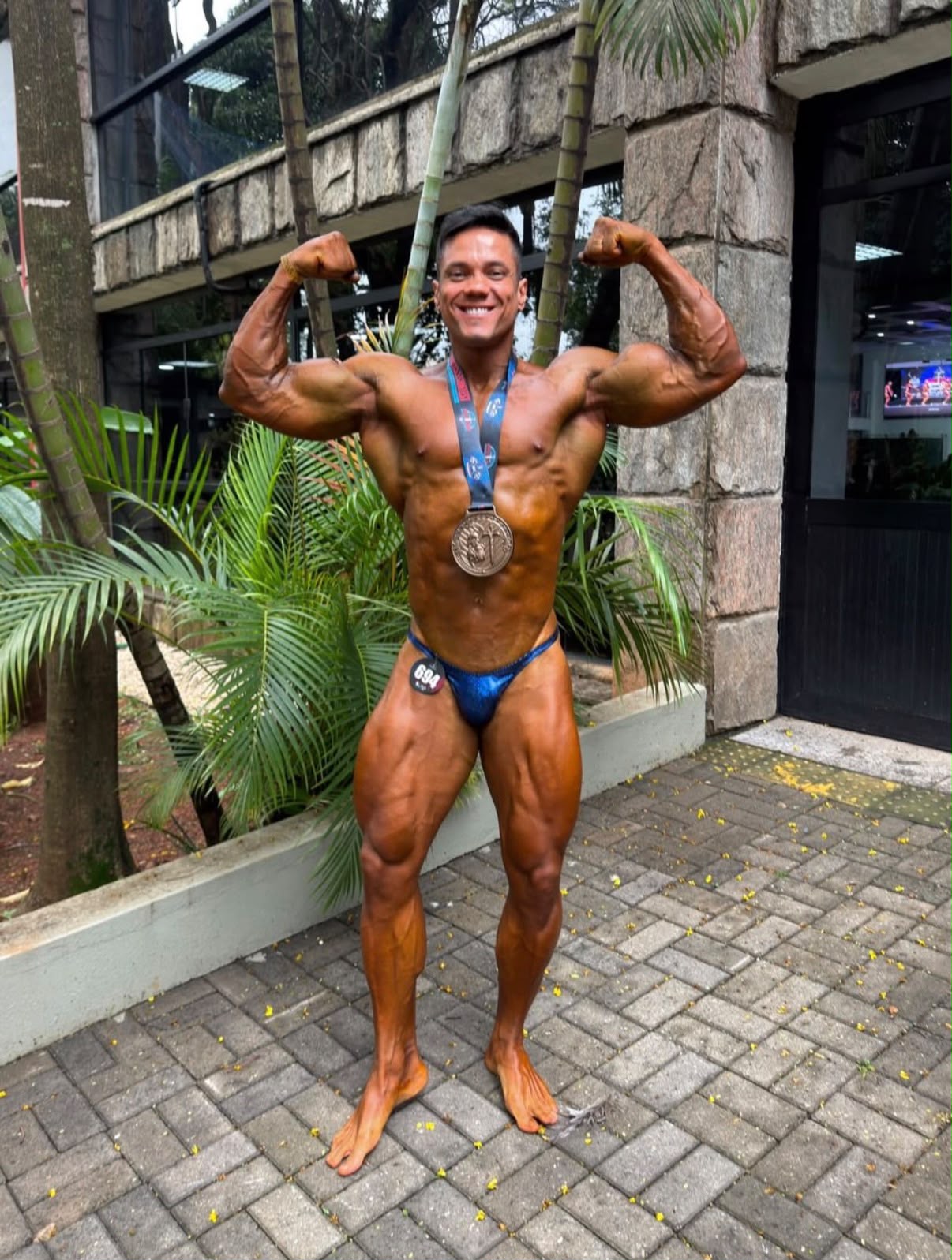Atleta com medalha, posando com os braços erguidos em área externa