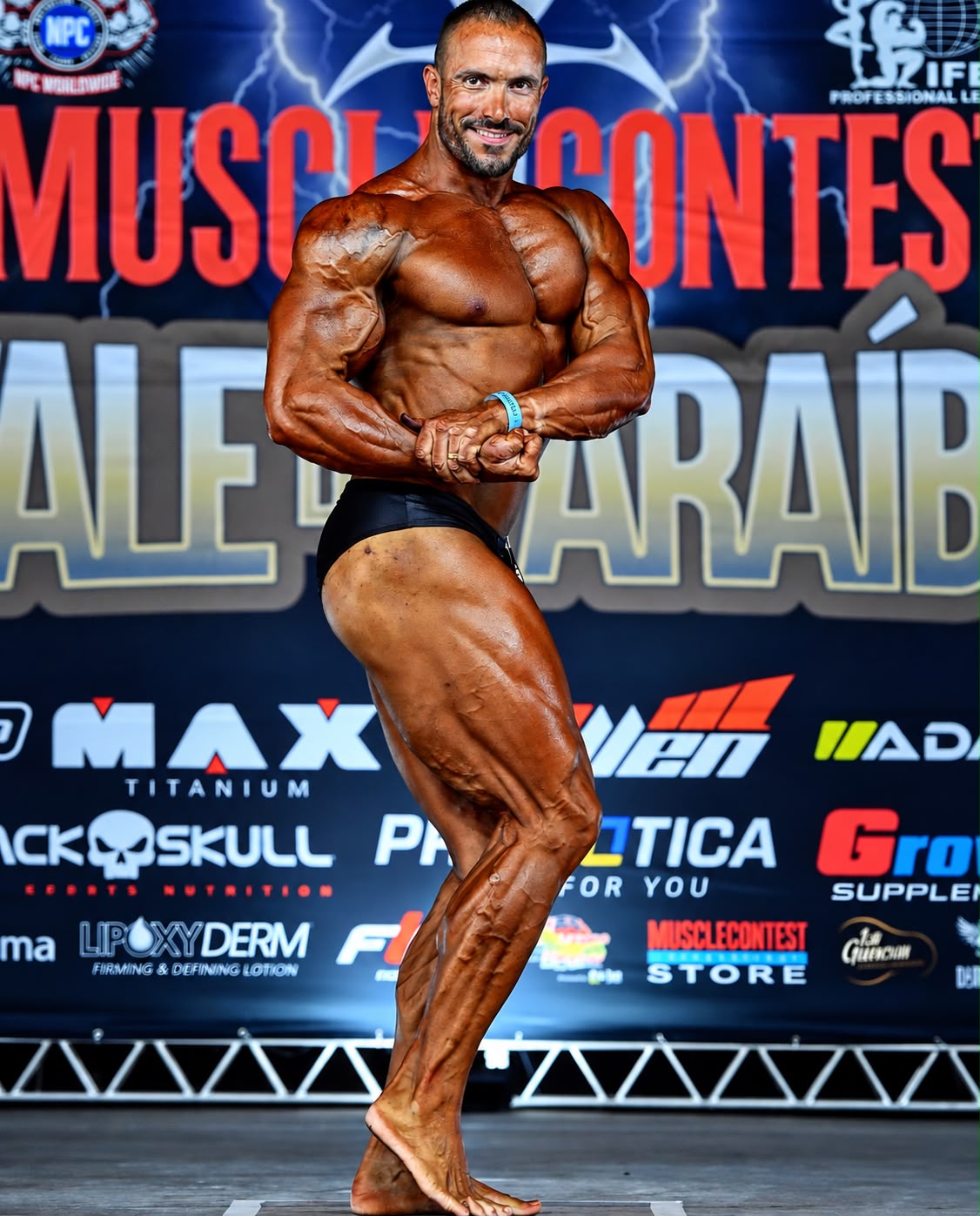 Atleta em pose lateral no palco de uma competição de fisiculturismo