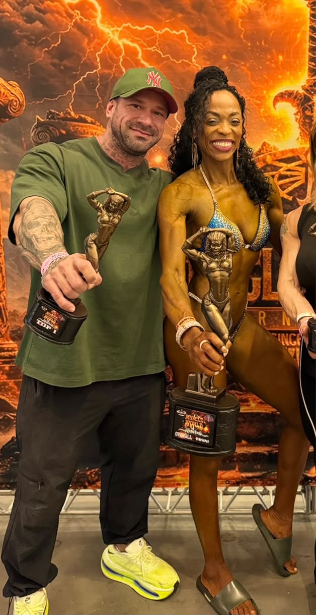 Joel de camiseta verde ao lado de uma atleta, ambos segurando troféus