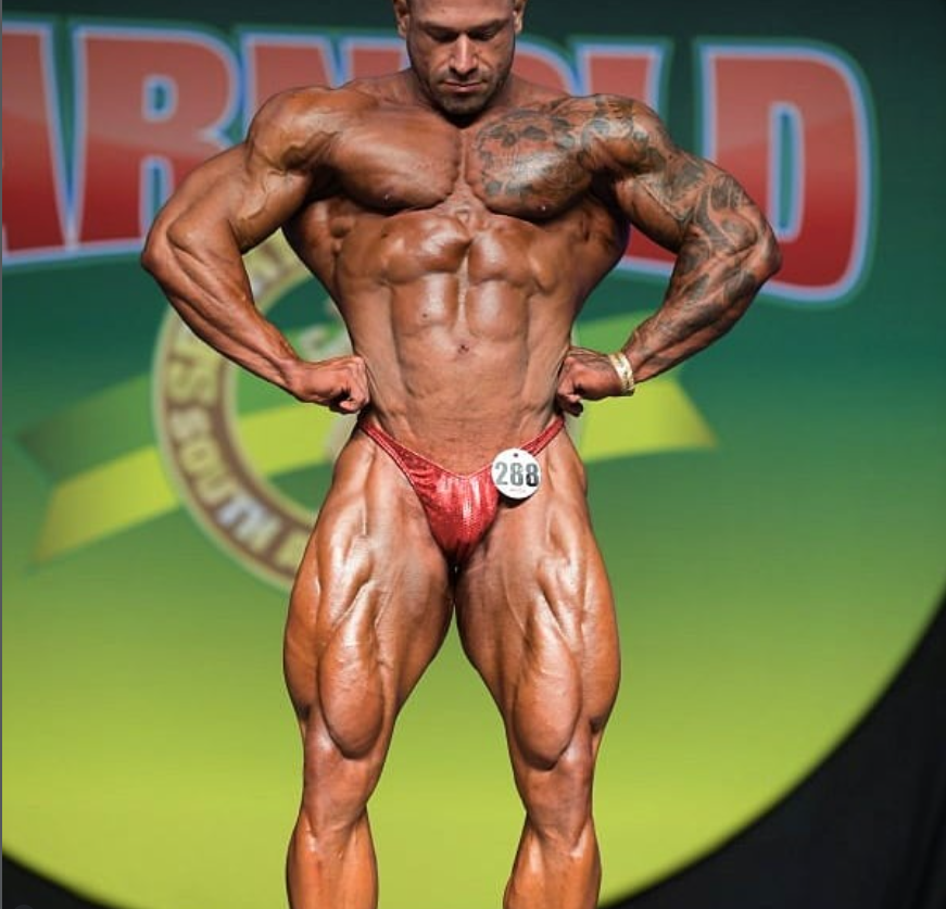 Joel Coutinho no palco de fisiculturismo, com traje vermelho e número 288